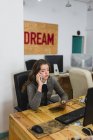 Ritratto di giovane donna con tablet e telefono parlante sul posto di lavoro — Foto stock