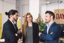 Woman looking at camera while men discussing in office. — Stock Photo