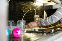 Crop image of female hands gathering water from tap in kitchen sink — Stock Photo