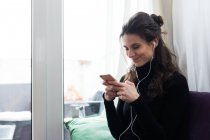 Portrait of smiling girl wearing earphones and chatting on smartphone — Stock Photo