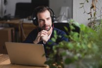 Portrait of man in headphones sitting at table with laptop looking at window — Stock Photo
