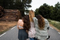 Three stylish girls sitting on rural road — Stock Photo