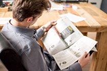 Visão traseira do empresário lendo jornal enquanto sentado na cadeira de escritório . — Fotografia de Stock