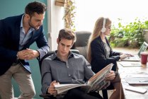 Two colleagues looking at newspaper while woman working — Stock Photo