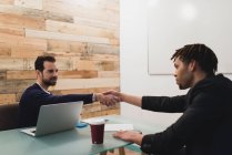 Side view of businessmen shaking hands over table at office — Stock Photo