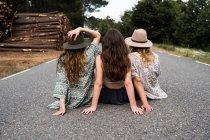 Tres chicas elegantes sentadas en el camino rural - foto de stock