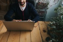 Обрезанное изображение человека в наушниках, сидящего за столом и использующего ноутбук — стоковое фото