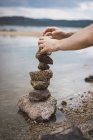 Hands stacking and balancing stones on lake shore. — Stock Photo