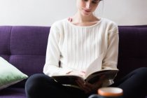 Crop image of brunette girl sitting on coach and reading book — Stock Photo