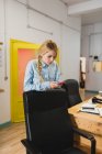 Портрет блондинки-бізнесу, що спирається на офісне крісло та перегляд смартфона — стокове фото