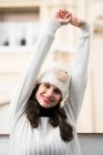 Smiling sleepy woman in knitted hat stretching and looking at camera. — Stock Photo