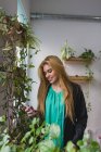 Retrato de rubia sonriente de pie cerca de plantas en maceta y el teléfono inteligente de navegación en la oficina - foto de stock
