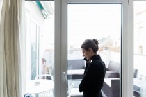 Vista lateral da mulher de pé perto da janela e telefone falando — Fotografia de Stock