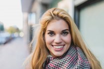 Portrait of smiling blonde woman looking at camera at street scene — Stock Photo