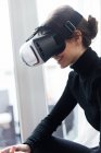 Vista lateral de chica morena con gafas de realidad virtual y jugando videojuego - foto de stock