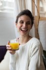 Femme riante tenant un verre de jus d'orange et regardant de côté — Photo de stock