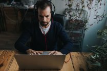 Retrato de homem em fones de ouvido sentado à mesa e usando laptop no local de trabalho do escritório — Fotografia de Stock