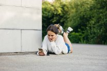 Menina que navega telefone enquanto deitado no chão — Fotografia de Stock