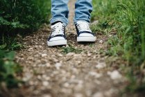 Legs of person wearing gumshoes standing on path in grass — Stock Photo
