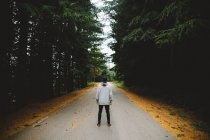 Visão traseira do homem em pé na estrada de asfalto solitário na floresta
. — Fotografia de Stock