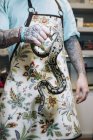 Tattooed man wearing apron holding big snake in hand. — Stock Photo