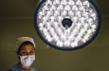 Médico femenino con máscara de pie sobre la lámpara - foto de stock