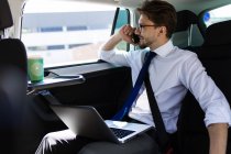 Человек с ноутбуком разговаривает по телефону в машине — стоковое фото