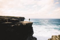 Вид сзади на человека, стоящего на вершине горной стены и смотрящего на морскую воду — стоковое фото