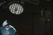 Хірург у масці, що працює під лампою — стокове фото