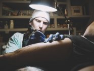 Portrait of master doing tattoo on client leg — Stock Photo