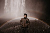 Молодой человек в пальто на водопаде — стоковое фото