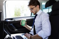 Homem com café e laptop no carro — Fotografia de Stock