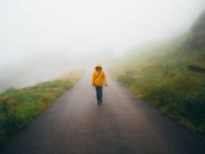 Female tourist in raincoat walking on foggy road — Stock Photo