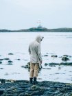 Mann an Steinküste gegen Leuchtturm auf Insel. — Stockfoto