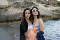 Модные девушки с цветным дымом на пляже — стоковое фото