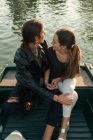 High angle of embracing couple sitting on boat and looking over shoulder — Stock Photo