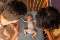 Overhead view of mother and father watching baby sleeping in crib — Stock Photo