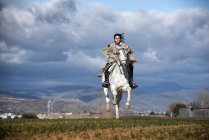 Frontansicht einer Frau, die auf einem laufenden Pferd auf einem Feld reitet — Stockfoto
