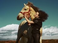Mujer joven sosteniendo caballo en el fondo del campo - foto de stock