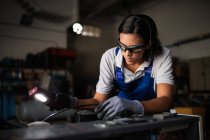 Porträt einer Mechanikerin, die Kompressormotor mit Taschenlampe inspiziert — Stockfoto