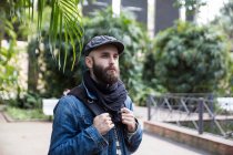 Portrait of bearded man in stylish outfit with backpack posing on background of street scene. — Stock Photo