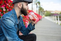 Vista lateral do homem bebendo smoothie com palha e olhando para longe . — Fotografia de Stock