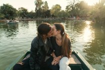Вид спереди на молодую пару, сидящую в лодке и целующуюся на озере — стоковое фото