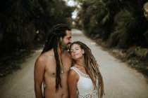 Портрет дівчини з дредлоками, що спираються на чоловіка без сорочки на тропічній алеї — стокове фото