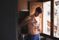 Oben-ohne-Mann füllt Tasse mit Kaffee in Küche. — Stockfoto
