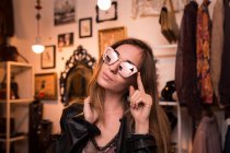 Молода стильна дівчина в творчих сонцезахисних окулярах позує на тлі кімнати одягу . — стокове фото