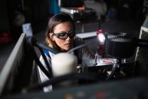Високий кут зору механіка-жінки в захисних окулярах, що перевіряє двигун компресора з ліхтариком — стокове фото