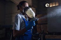 Vue latérale du mécanicien féminin portant un respirateur à l'aide d'un pistolet pulvérisateur — Photo de stock