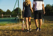 Crop coppia a piedi sul campo da tennis illuminato dal sole — Foto stock
