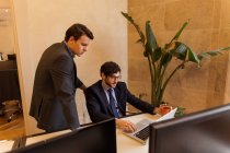 Zwei junge Männer in Anzügen schauen auf Laptop im Büro. — Stockfoto
